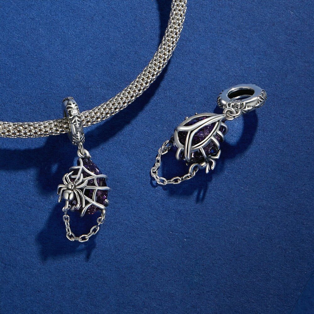 Sterling silver spider charm with violet crystal, web cage, and chain detail.