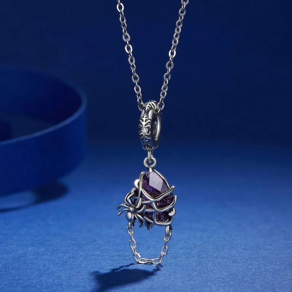 Sterling silver spider charm with violet crystal, web cage, and chain detail.