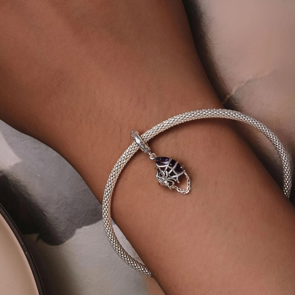 Sterling silver spider charm with violet crystal, web cage, and chain detail.