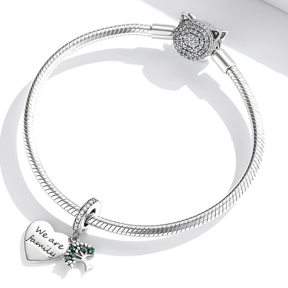 Sterling silver heart charm engraved “We are family” with green gemstones and cross detail.