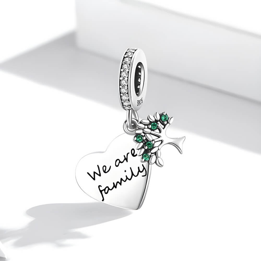 Sterling silver heart charm engraved “We are family” with green gemstones and cross detail.