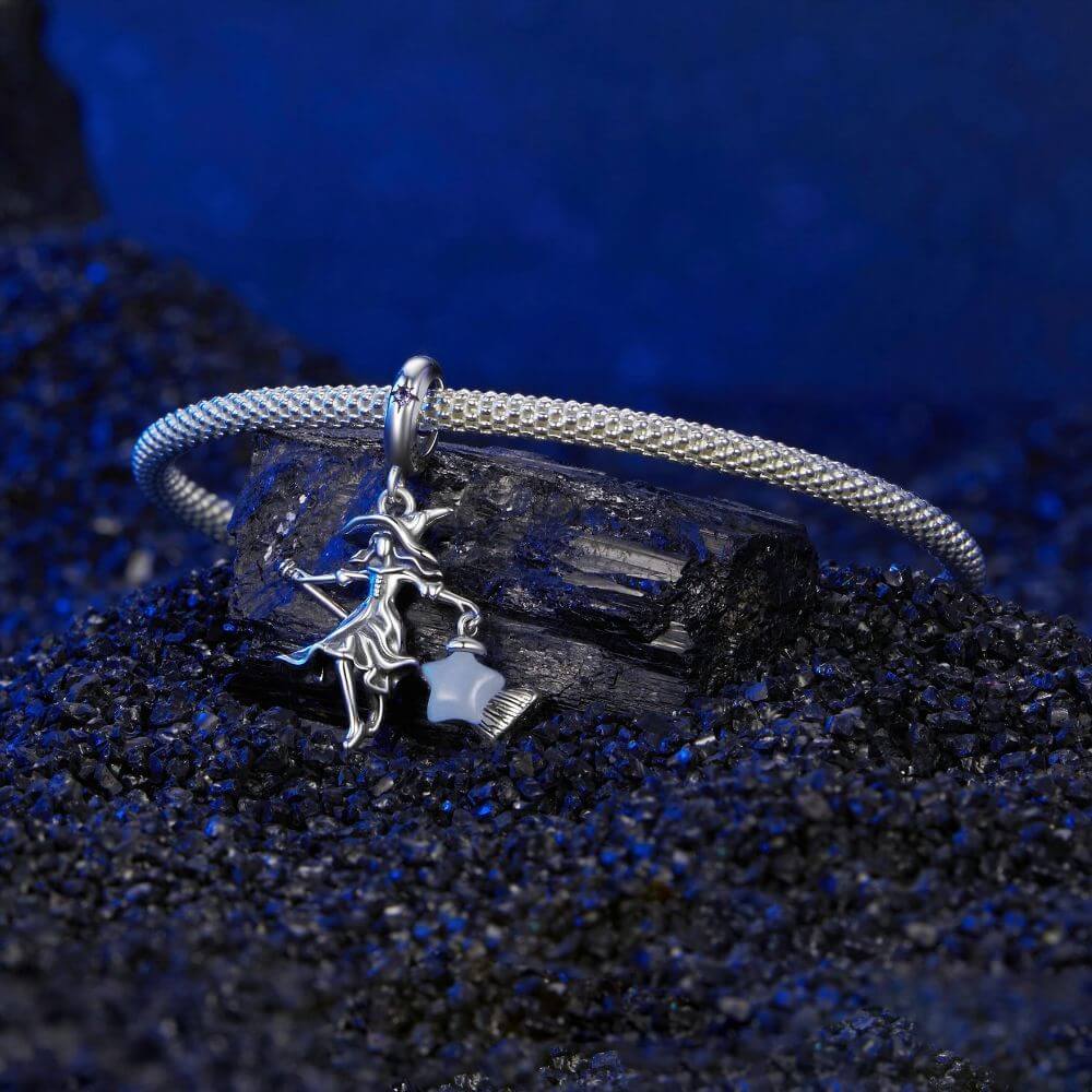 Sterling silver witch charm with broomstick, flowing dress, purple crystal, and glowing blue star lantern.