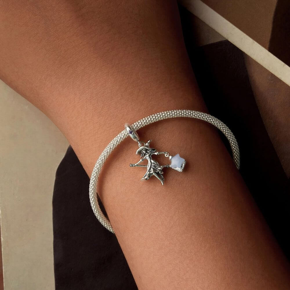 Sterling silver witch charm with broomstick, flowing dress, purple crystal, and glowing blue star lantern.